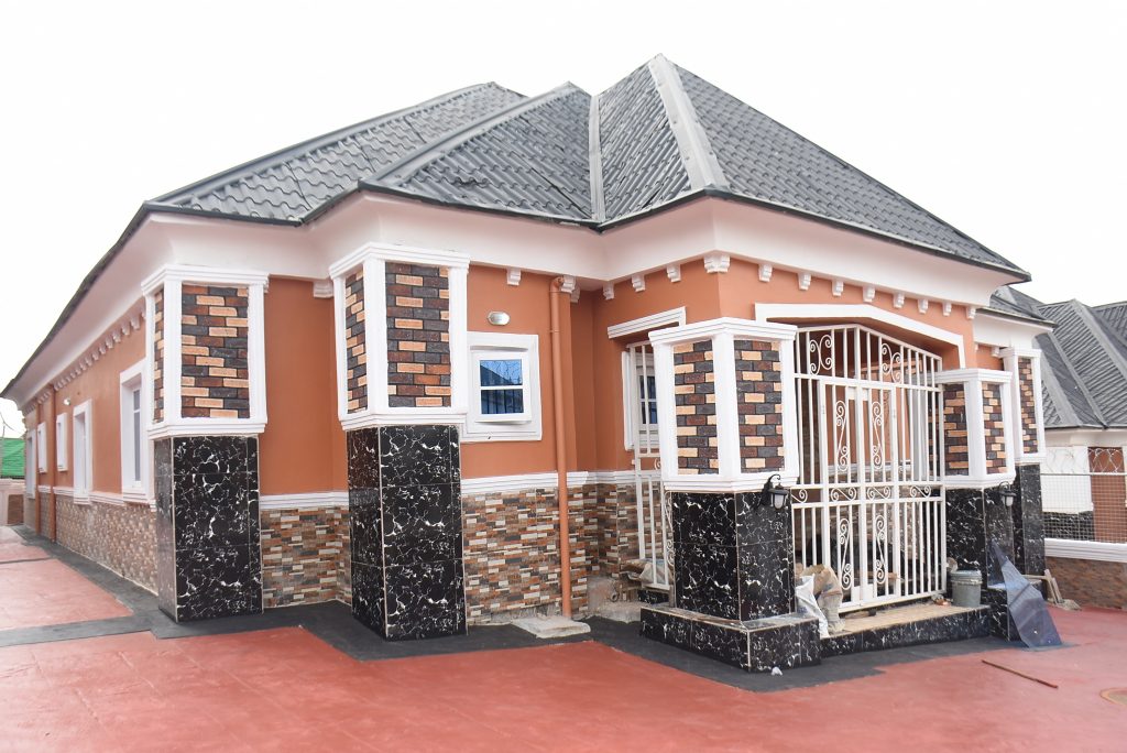 Close-up of a finished bungalow facade with stone-clad columns and a wrought-iron gate